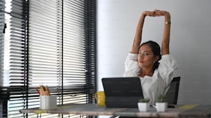 A calm smiling businesswoman is relaxing at comfortable office chair and stretching raising hands up.