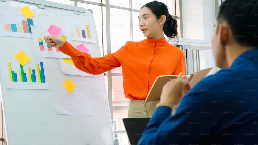 Jovem explica dados de negócios em quadro branco em sala de escritório casual. A confiante empresária asiática relata o progresso das informações de um projeto de negócios para se associar para determinar a estratégia de mercado.