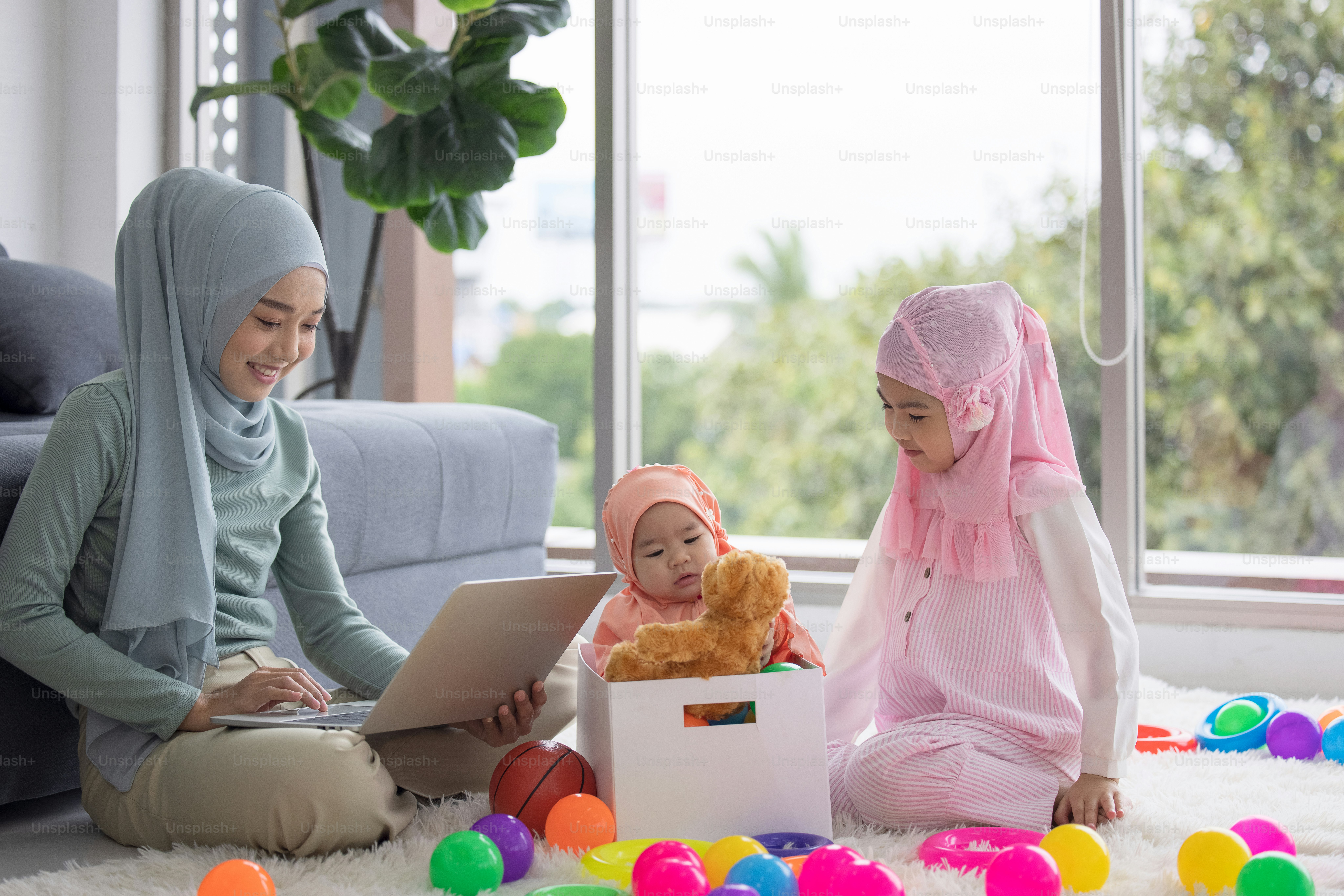 Muslim Mother working with laptop and Cute little baby playing toys in living room at home.