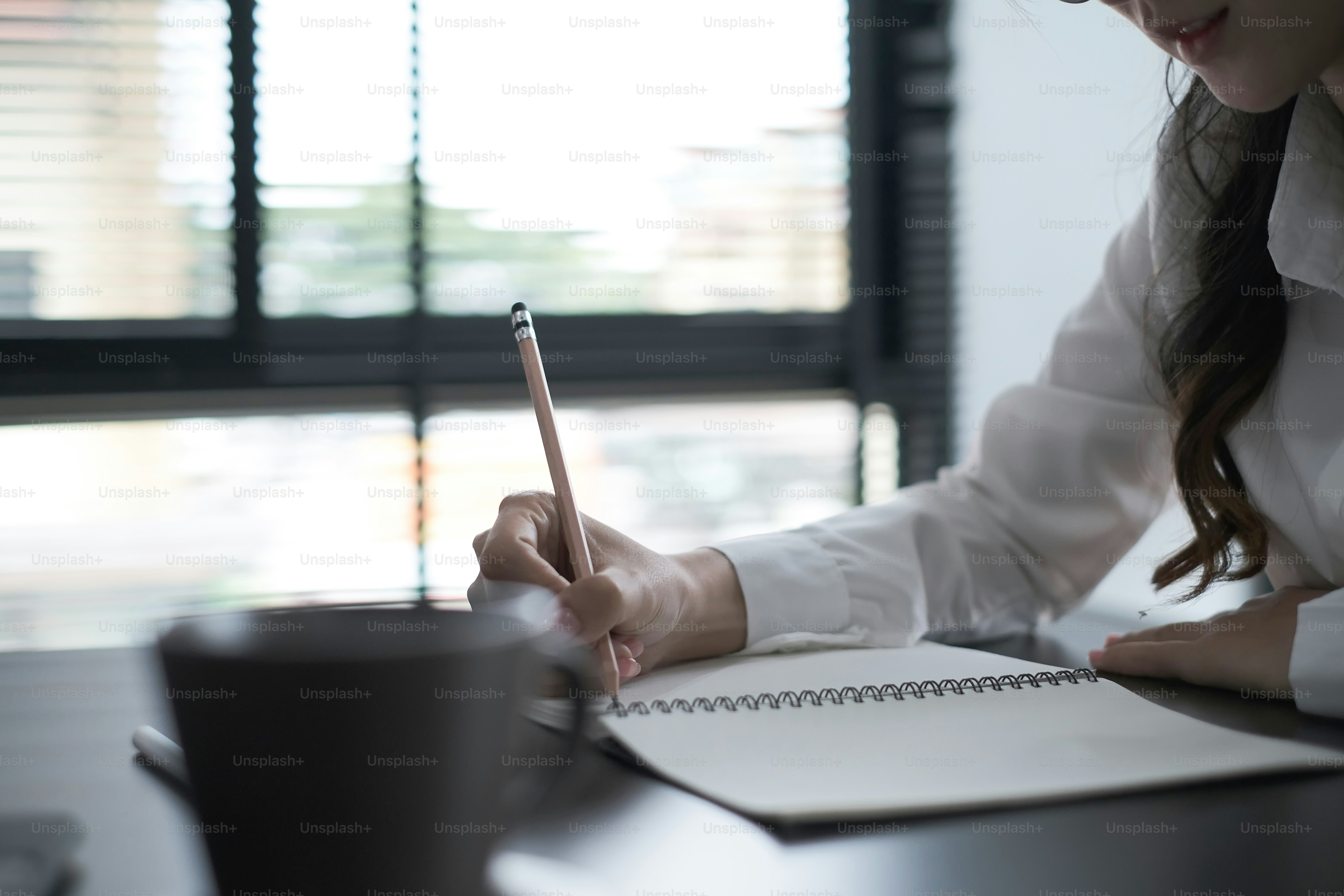 Una donna d'affari lavora in ufficio tenendo in mano penne e prendendo appunti su un taccuino sul tavolo.