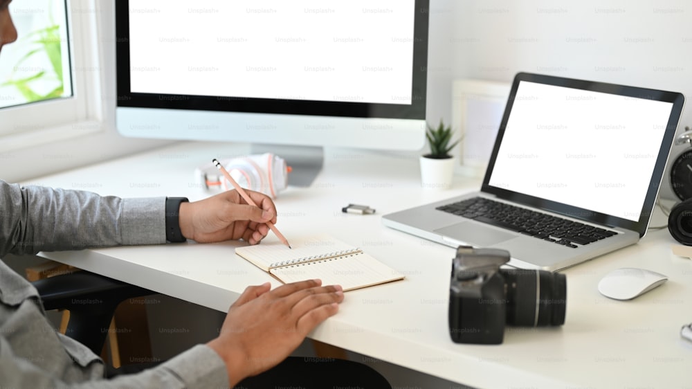 Cropped shot of graphic designer or photographer is writing on a blank notebook on the table.