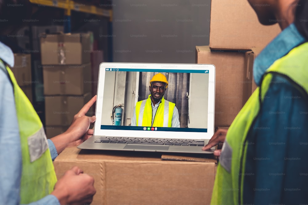 Warehouse staff talking on video call at computer screen in storage warehouse . Online software technology connects people working in logistic factory by virtual conference call on internet network .