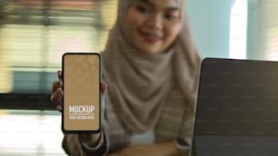 Nahaufnahme der muslimischen Frau zeigt Mock-up-Smartphone-Bildschirm, einschließlich Clipping-Pfad