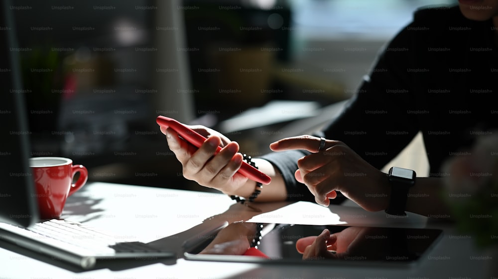 Foto cortada de um jovem designer gráfico usando smartphone em sua mesa no escritório moderno.