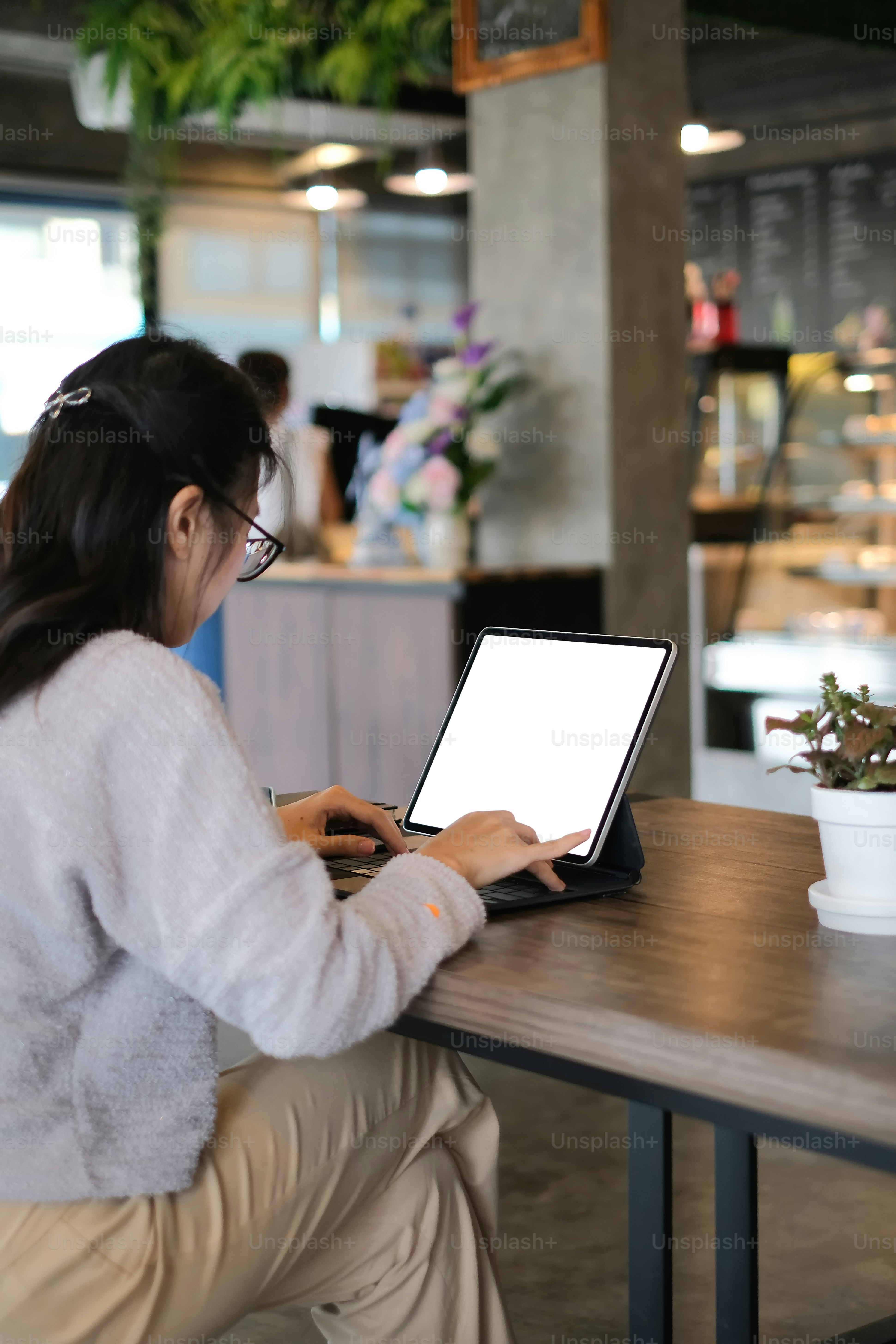 Hind viewof a young businesswoman is working with computer tablet in modern cafe.