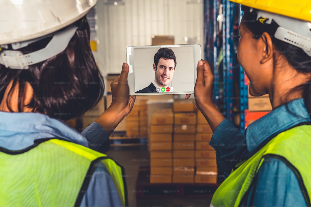 Warehouse staff talking on video call at computer screen in storage warehouse . Online software technology connects people working in logistic factory by virtual conference call on internet network .