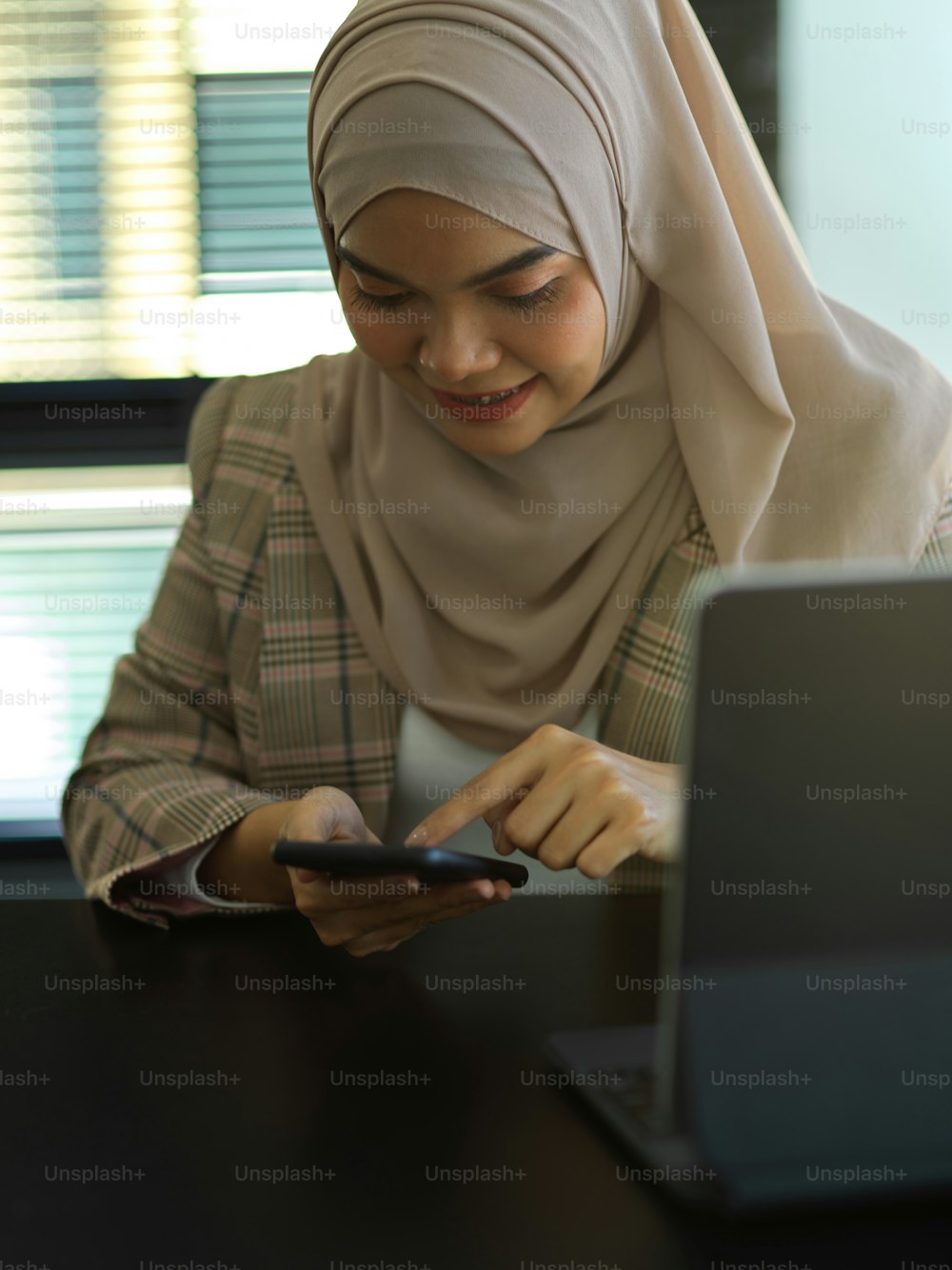 Porträt einer asiatischen muslimischen Geschäftsfrau mit Smartphone bei der Arbeit mit Tablet im Büro