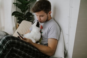 Handsome man sitting with cat and holding phone in hand in stylish modern room. Cute cat playing with owner and attracting attention from smartphone