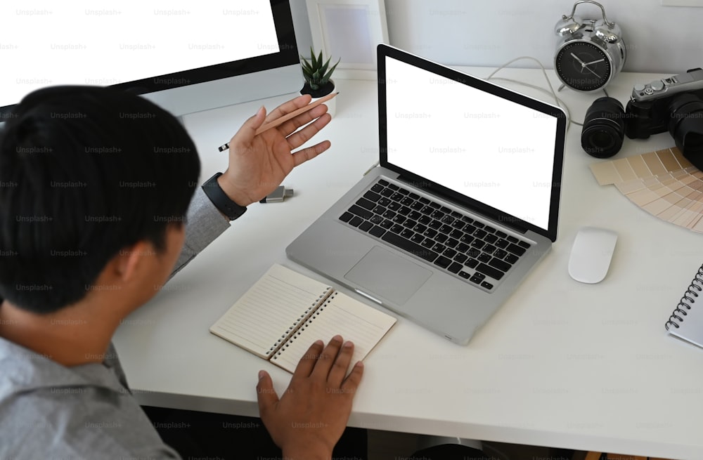 Vue aérienne d’un graphiste ou d’un photographe travaillant avec un ordinateur portable sur une table blanche.