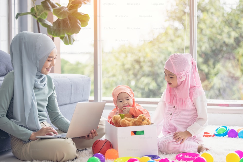 Muslim Mother working with laptop and Cute little baby playing toys in living room at home.
