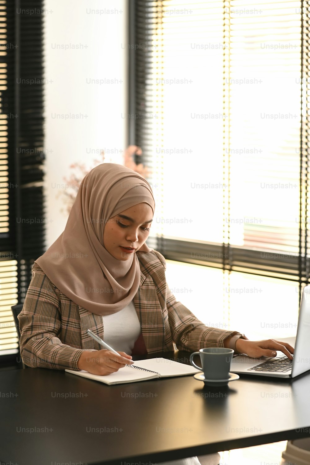 Portrait of young Arabic business woman wearing hijab is taking notes in notebook at her office.