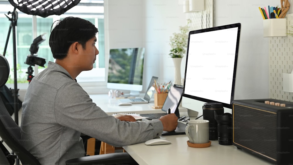 Vista lateral do designer gráfico ou fotógrafo está usando mesa gráfica retocando uma foto em seu espaço de trabalho.