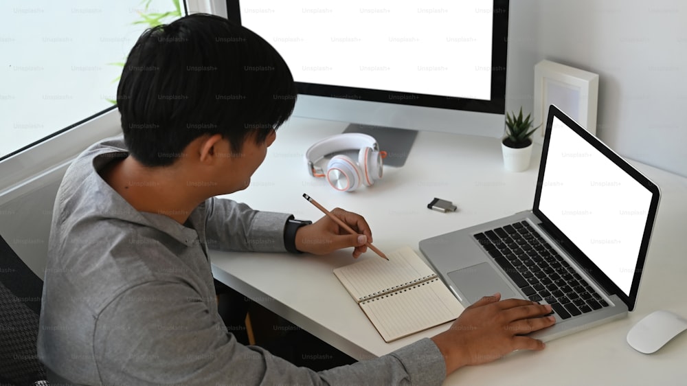 그래픽 디자이너 또는 사진 작가의 잘린 샷은 테이블에 앉아 노트북에 메모를 하고 있습니다.