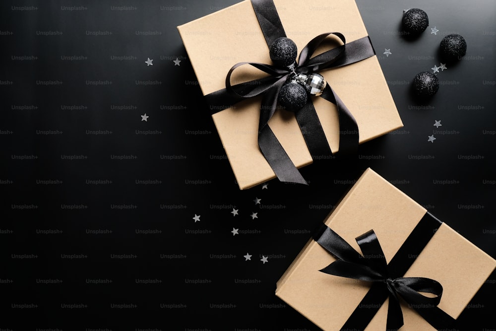 Scatole regalo natalizie di lusso con fiocco a nastro e palline su sfondo nero. Concetto di vendita natalizia o del Black Friday. Posa piatta, vista dall'alto.
