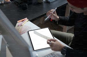 Foto cortada de designer gráfico criativo masculino está trabalhando em amostras de cores e desenhando em tablet gráfico no local de trabalho com ferramentas de trabalho e acessórios.