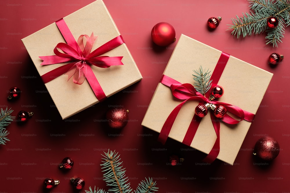 Boîtes cadeaux de Noël et branches de sapin avec décoration de boules sur fond rouge marsala. Cadeaux de Noël, surprises. Pose à plat, vue de dessus.