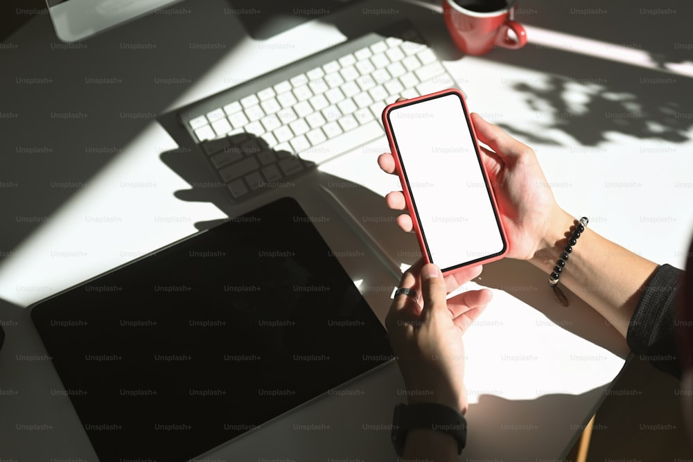 Over head shot of woman holding mobile phone mockup while sitting on her workspace. Blank screen for graphic display montage.