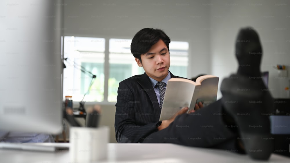 An Asian attractive businessman relaxing at his workspace and putting legs on table in office.