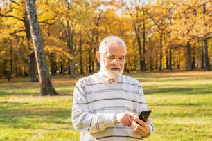 Elderly senior man using smart phone outside in autumn park.