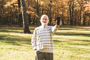 Älterer älterer Mann, der draußen ein Smartphone benutzt, zeigt einen leeren Bildschirm des Mobiltelefons.