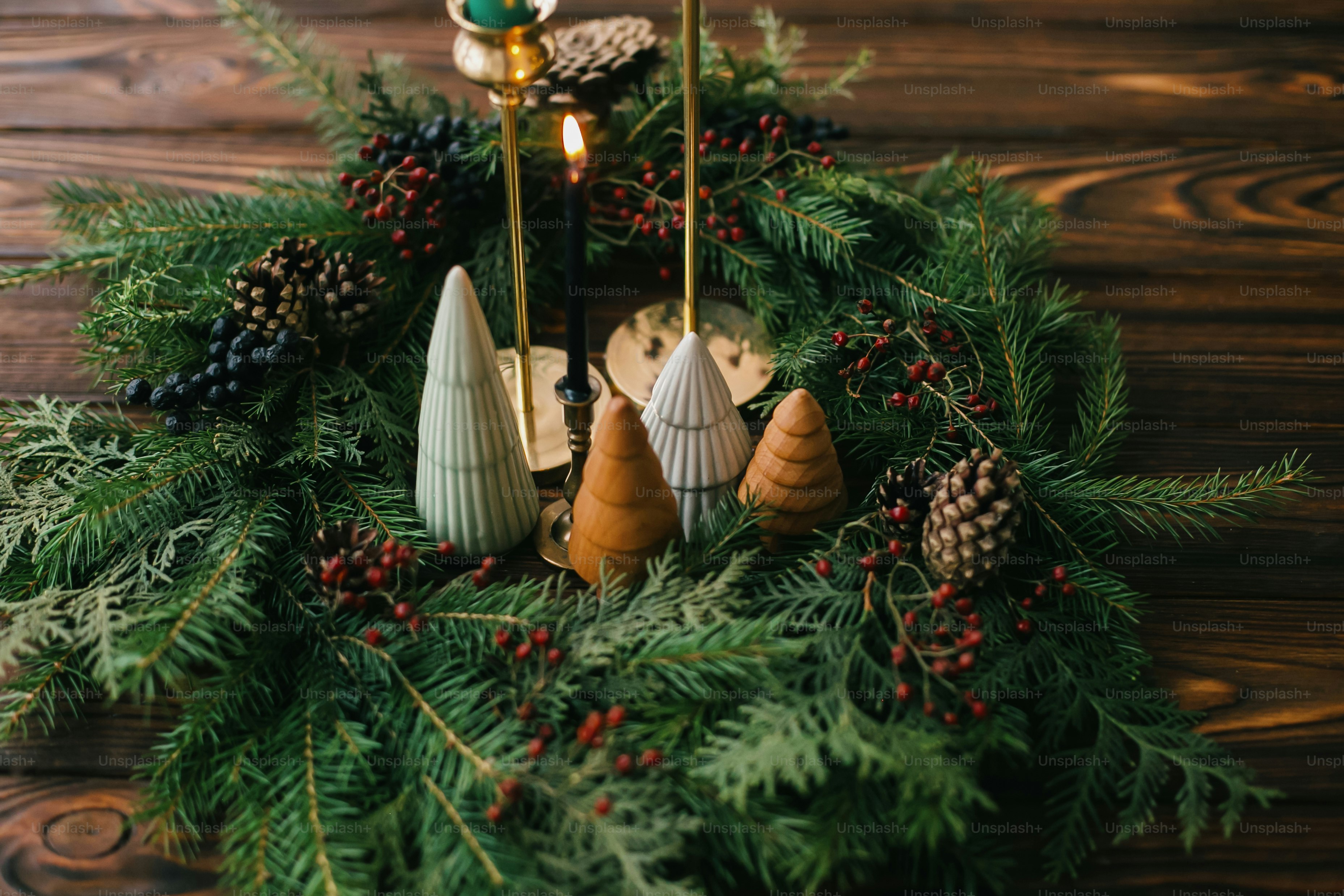 Merry Christmas! Modern handmade wreath with little trees, candles and pine cones on rustic wooden table, christmas table setting. Festive stylish decor for holiday dinner at home.