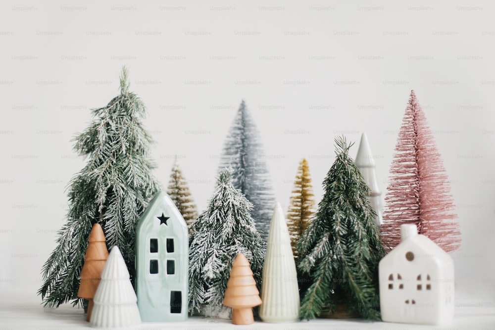 Merry Christmas! Christmas scene, miniature holiday village. Christmas little ceramic houses, wooden and snowy fir trees on white background. Festive modern decorations.