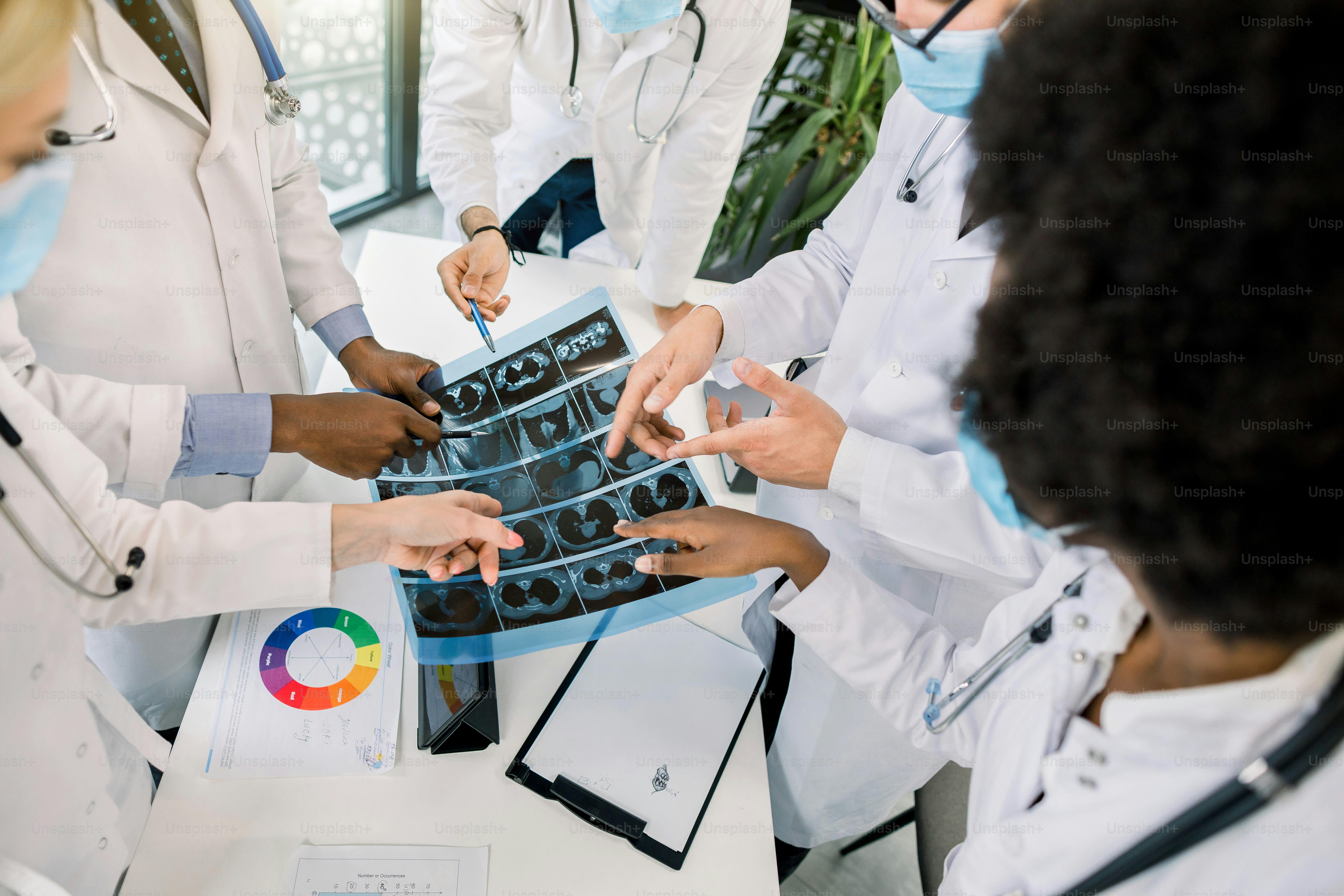 Computed tomography concept, covid 19 pandemy. Close up cropped top angle image of multiracial group of doctors looking at X-ray CT scan of lungs and discussing the diagnosis and treatment.