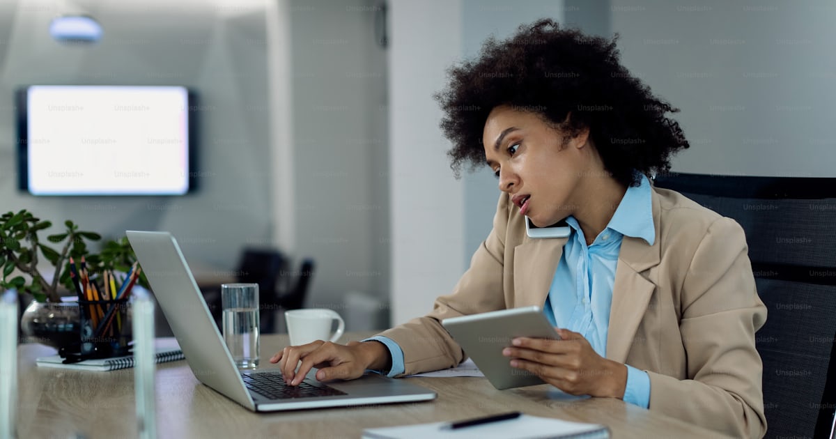Multi-tasking black businesswoman working on laptop while using ...