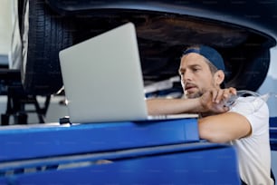 Mid adult car mechanic working on laptop at auto repair shop.