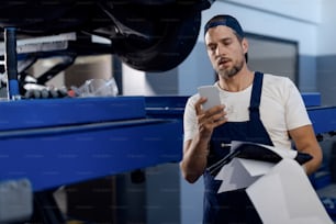 Auto repairman using cell hone and text messaging while working in a workshop.