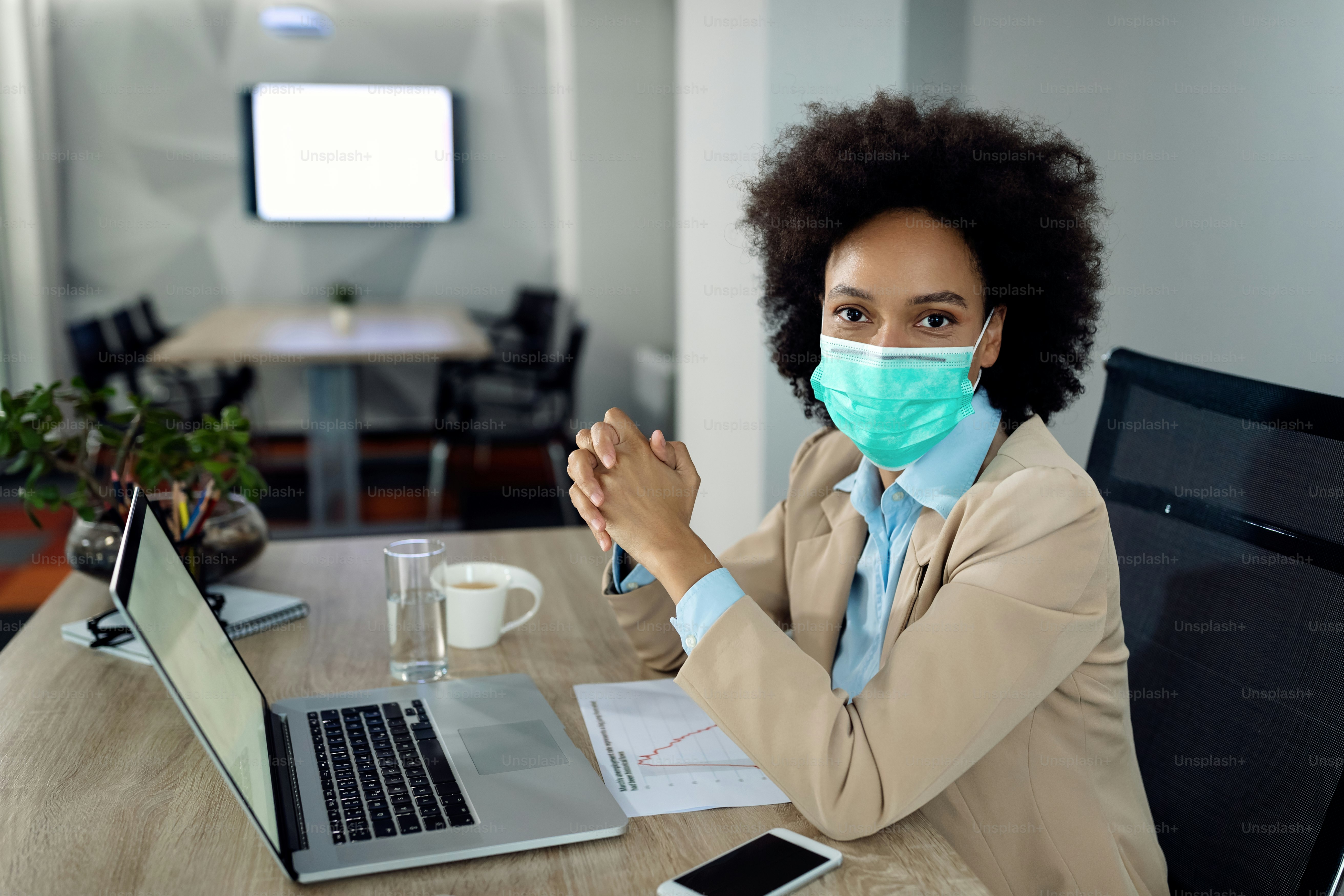 African American businesswoman working on a computer and her office desk and wearing face mask due to COVID-19 pandemic.