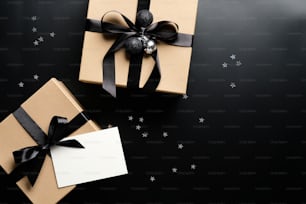 Christmas presents with ribbon bow and empty paper card on black background with confetti. Christmas gifts, seasonal holidays greetings concept.