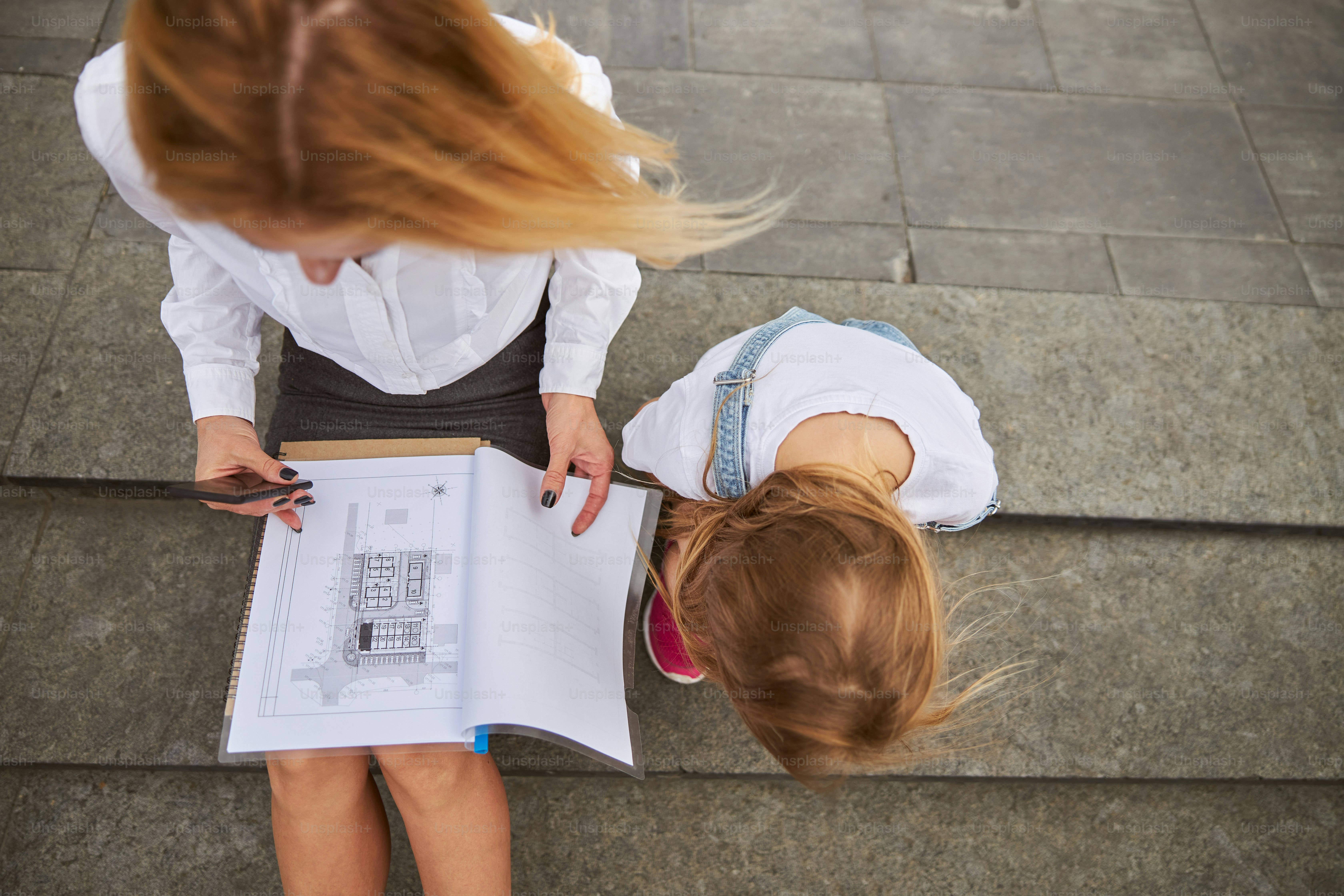 Top view portrait of business lady working with documents while sitting on the steps with female child in the outdoors