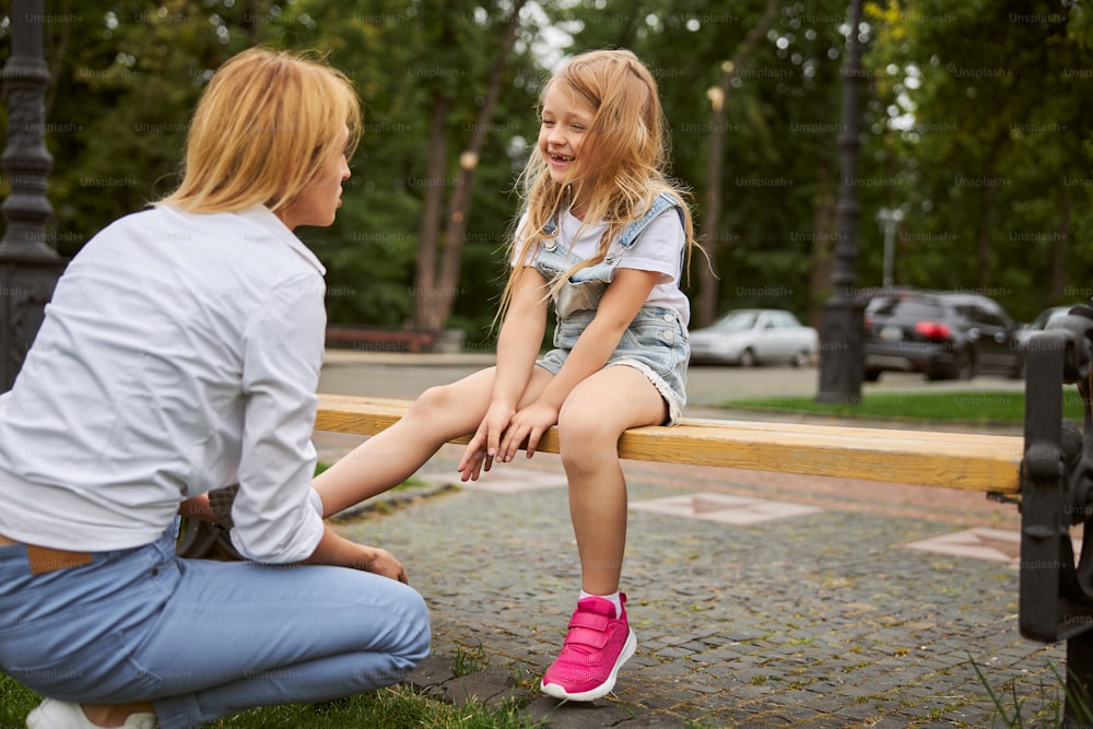 Close up portrait of woman talking with little girl while sitting on the wooden bench