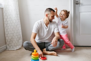 Young Caucasian father playing with child girl. Male man parent entertains toddler daughter sitting at home. Authentic lifestyle candid moment. Happy dad family day life concept.