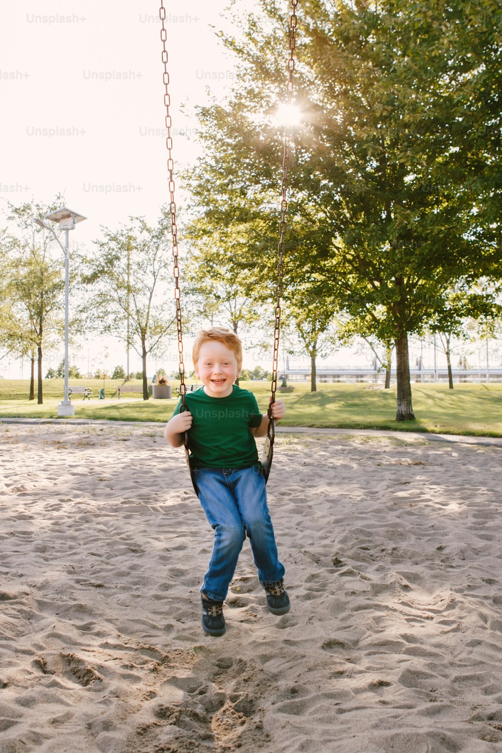 夏の日に外のブランコセットの遊び場でスイングする幸せな笑顔の小さな就学前の男の子。幸せな子供時代のライフスタイルのコンセプト。子供向けの季節の野外活動。