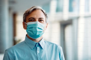 Empresário adulto usando máscara facial no escritório devido à pandemia de coronavírus e olhando para a câmera.