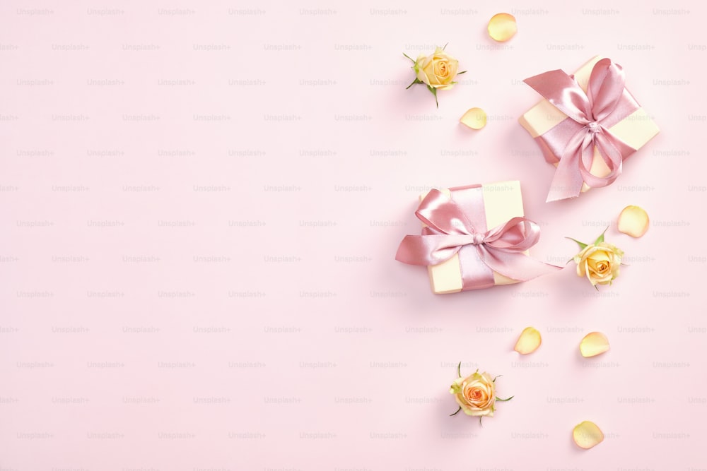 パステルピンクの背景にピンクのリボン、弓、黄色のバラ、花びら、つぼみのギフトボックス。バレンタインデー、母の日、誕生日のコンセプト。ミニマルなスタイル。