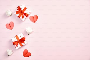 Joyeux concept de la Saint-Valentin. Coffrets cadeaux avec noeud de ruban rouge, fleurs de roses, coeurs en papier sur fond rose pastel. Maquette de carte de voeux Saint Valentin.