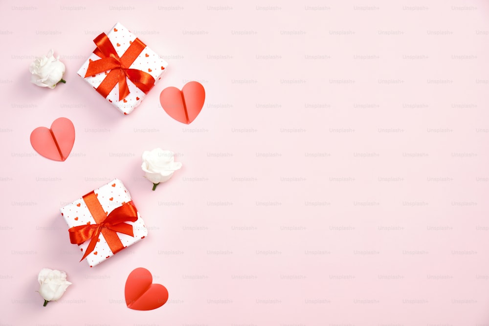 Happy Valentines day concept. Gift boxes with red ribbon bow, roses flowers, paper hearts on pastel pink background. Valentines day greeting card mockup.