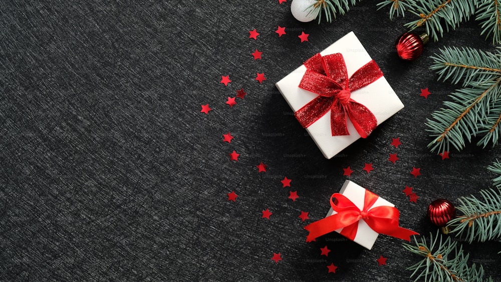 Elegante Weihnachtsgeschenkboxen mit roten Bandschleifen, Tannenzweigen, funkelndem Konfetti auf schwarzem Hintergrund. Weihnachtsbanner-Design, Neujahrsgrußkarten-Mockup, Header-Vorlage.