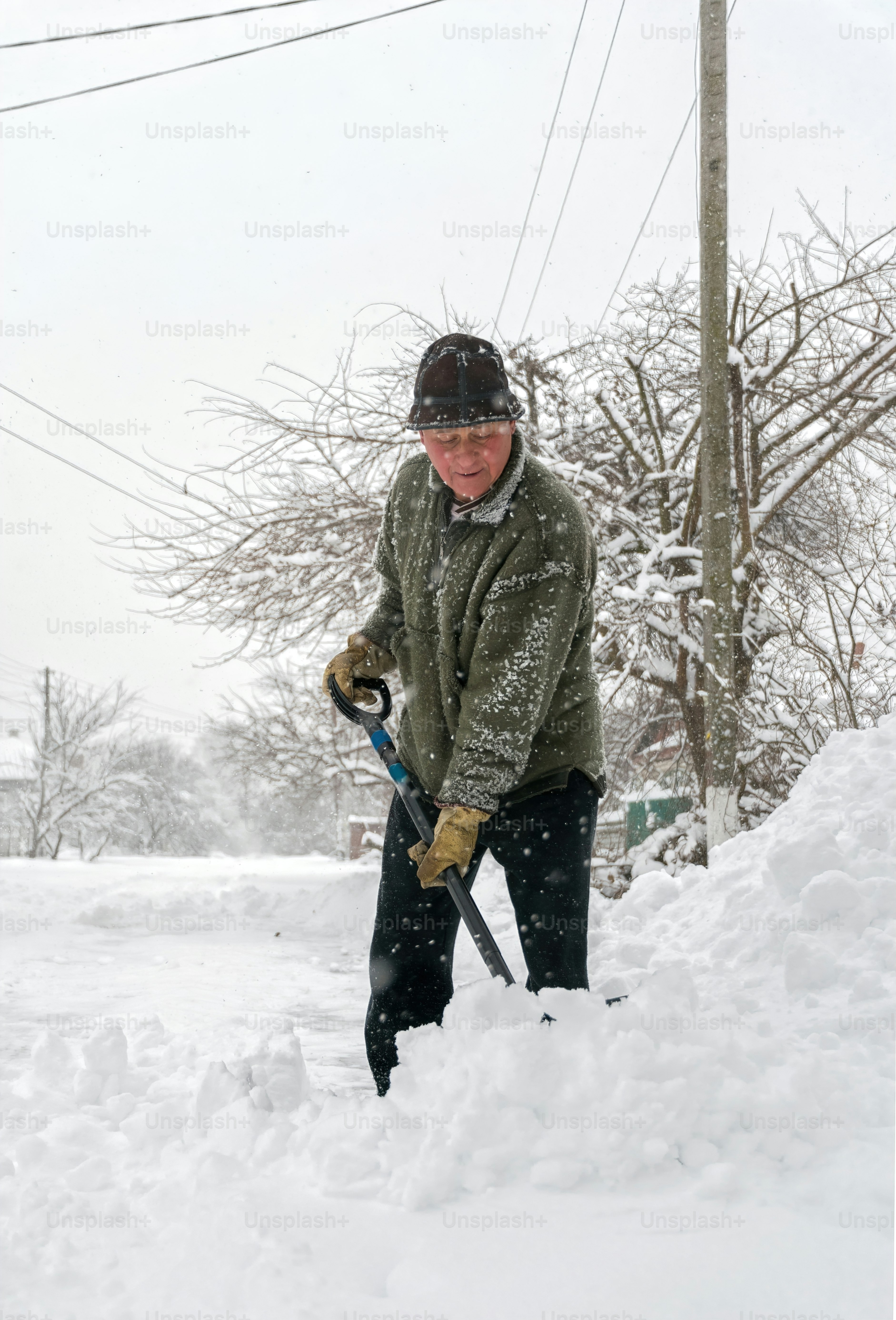 elderly man with a shovel in his hands clears the street after a heavy snowfall. Man at seasonal work