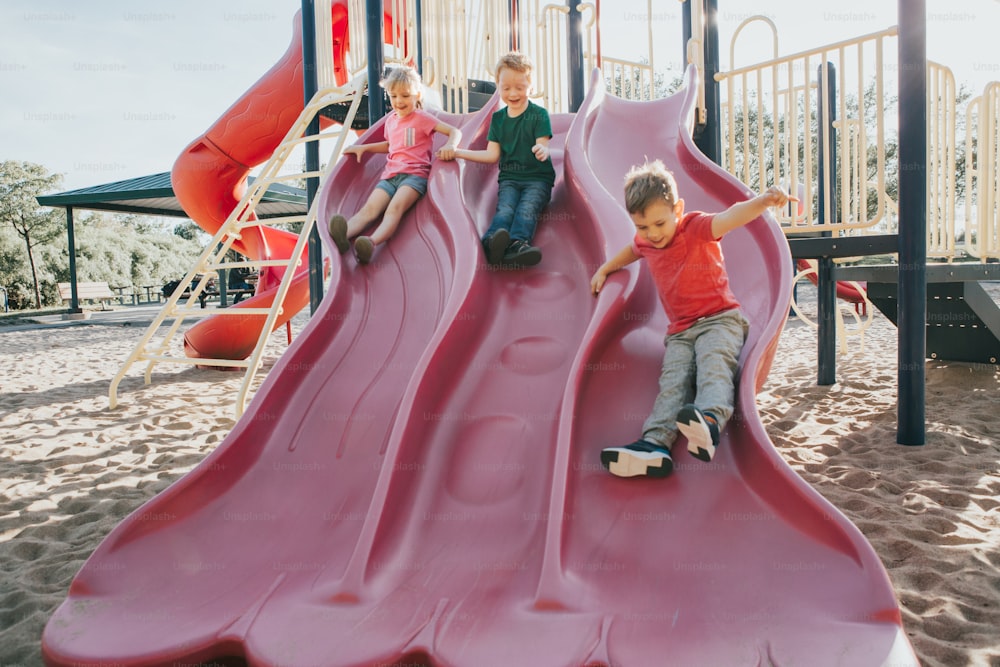 Active happy Caucasian children sliding on playground schoolyard outdoor on summer sunny day. Kid friends boys girl having fun. Seasonal kids activity outside. Authentic childhood lifestyle concept.