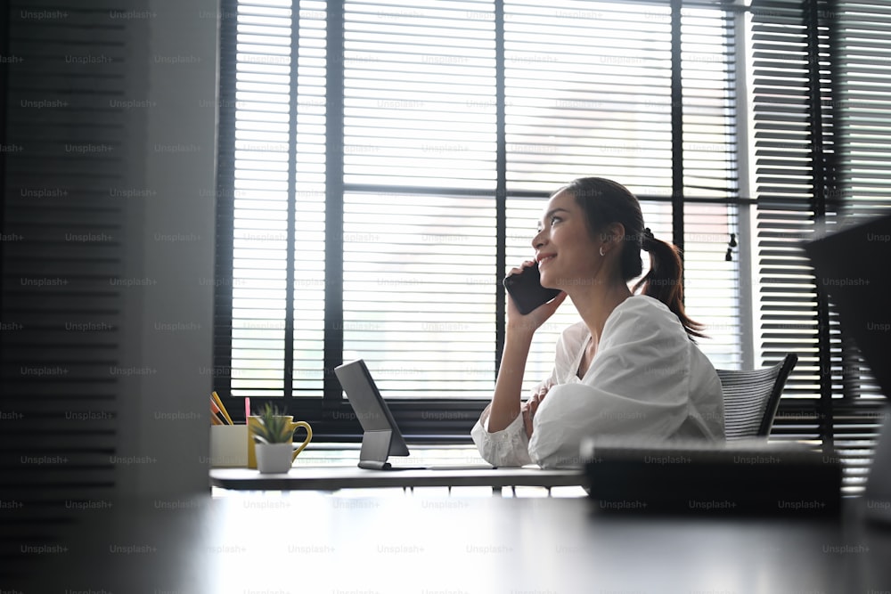 Smiling business woman sitting at her desk working and talking on the phone.