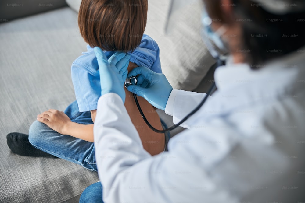 Beschnittenes Foto eines Arztes im Laborkittel, der ein Stethoskop verwendet, um auf die Überprüfung der Kinderlunge zu hören