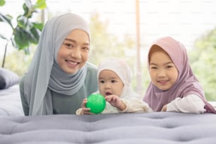 Muslimische Mutter im Hijab ist ihre kleine Tochter, die im Wohnzimmer sitzt, liebevolle Beziehung