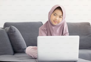 Asiatischer muslimischer Teenager Surfen Internet mit Notebook auf dem Sofa im Wohnzimmer