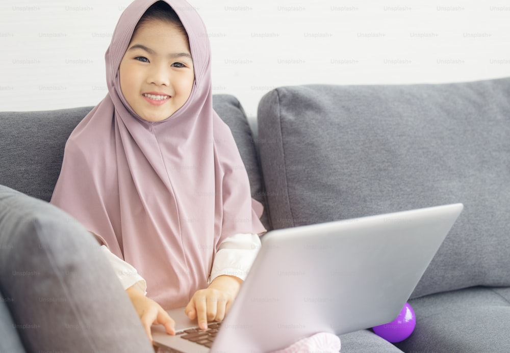 Asiatico musulmano Adolescente che naviga in Internet con il taccuino sul divano in soggiorno