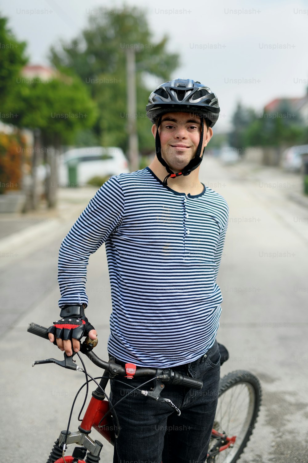 Porträt eines erwachsenen Mannes mit Down-Syndrom und Fahrrad, der draußen auf der Straße steht und in die Kamera schaut.