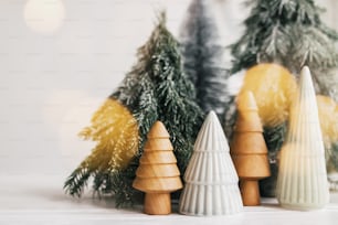 Scène de Noël, forêt d’hiver miniature en lumières. Petits sapins de Noël en céramique, en bois et enneigés sur fond blanc avec illumination. Décoration moderne et festive. Joyeux Noël!